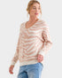 Woman wearing a beige and white patterned sweater with blue jeans on a white background