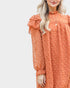 Woman wearing an orange dress with ruffled sleeves against a white background