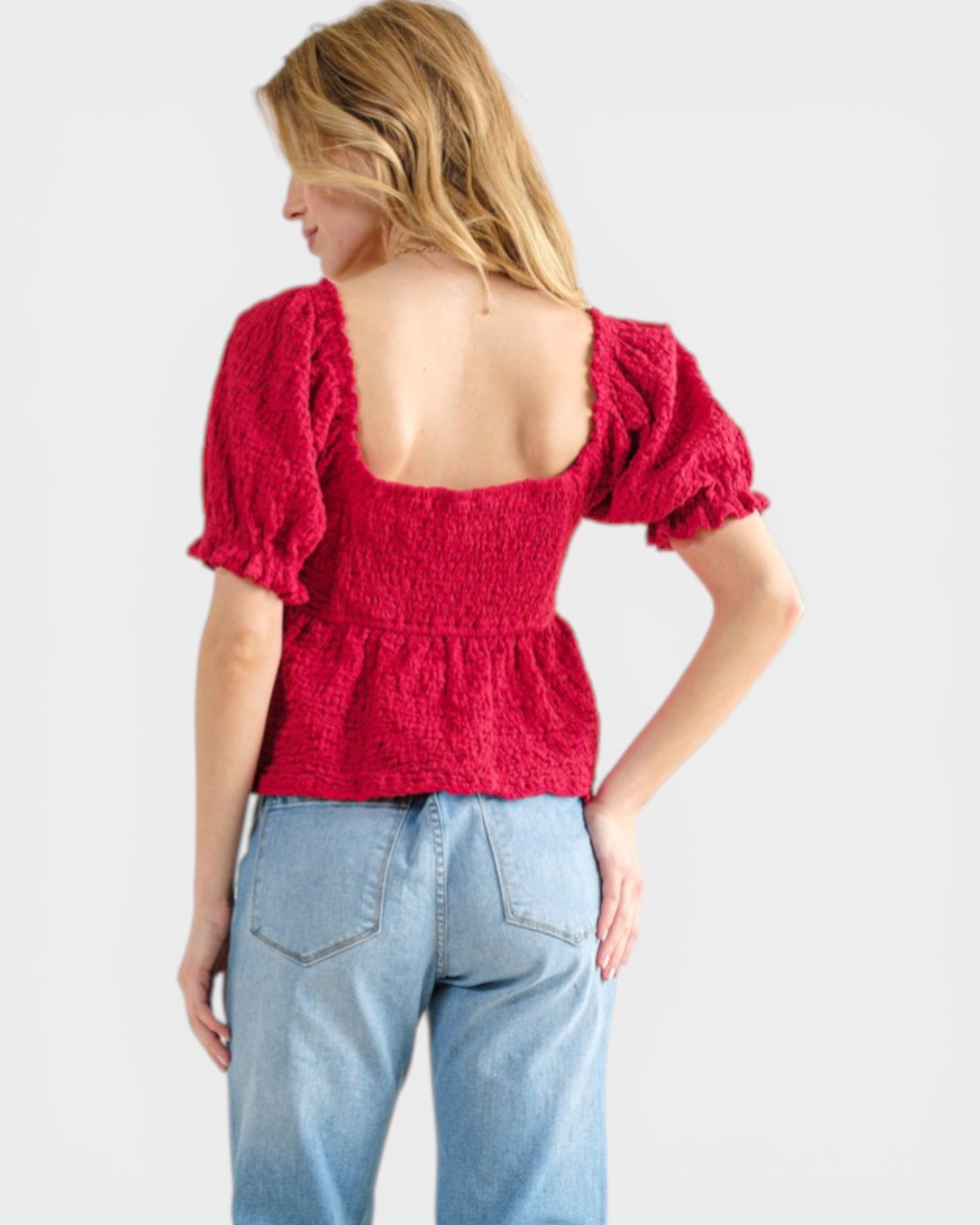 Woman wearing a red top with puff sleeves and light blue jeans on a white background