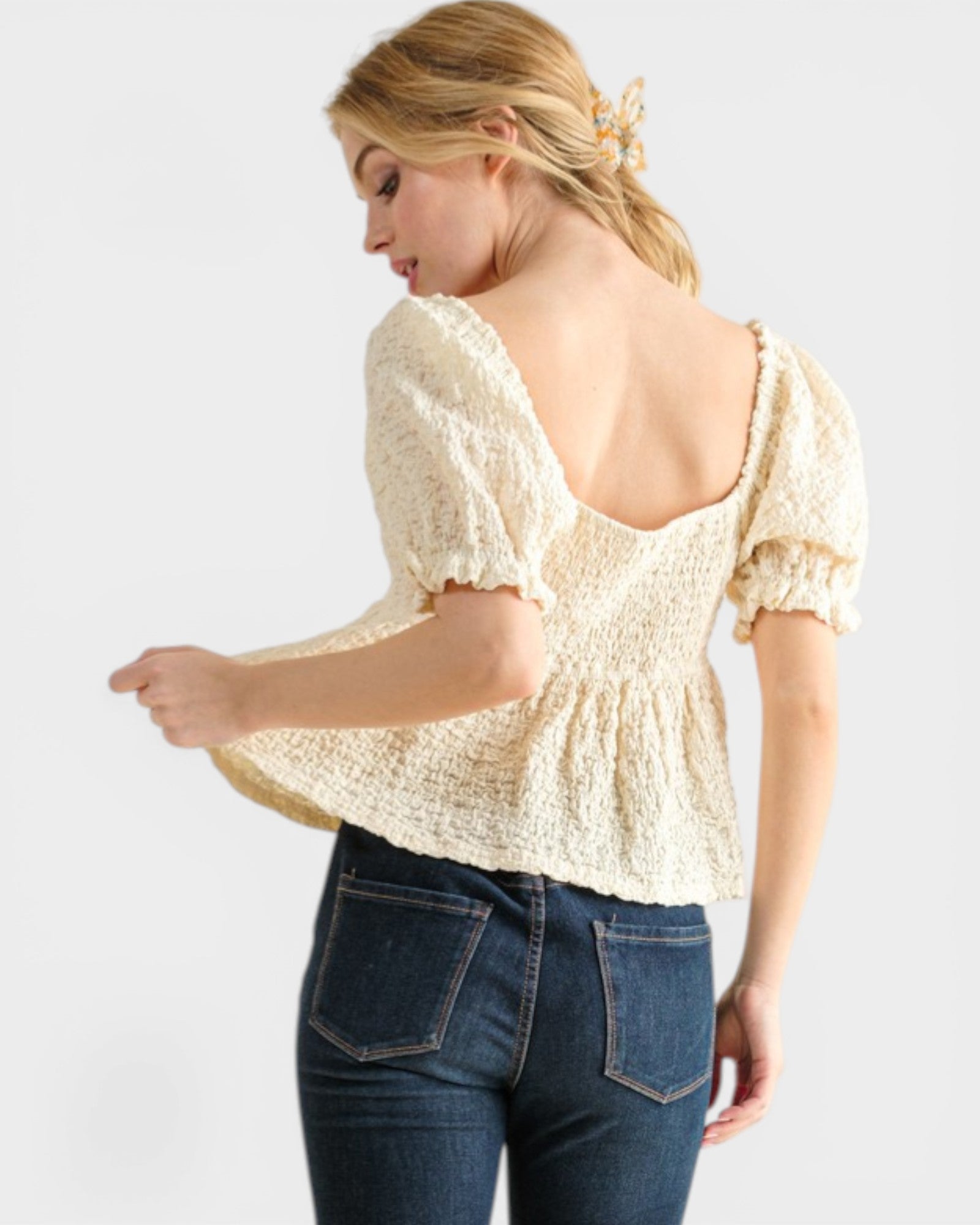 Woman wearing a light yellow blouse with short sleeves and blue jeans on a white background