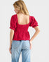 Woman wearing a red top with puff sleeves and light blue jeans on a white background