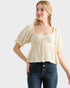 Woman wearing a light-colored blouse with short sleeves and dark jeans on a white background