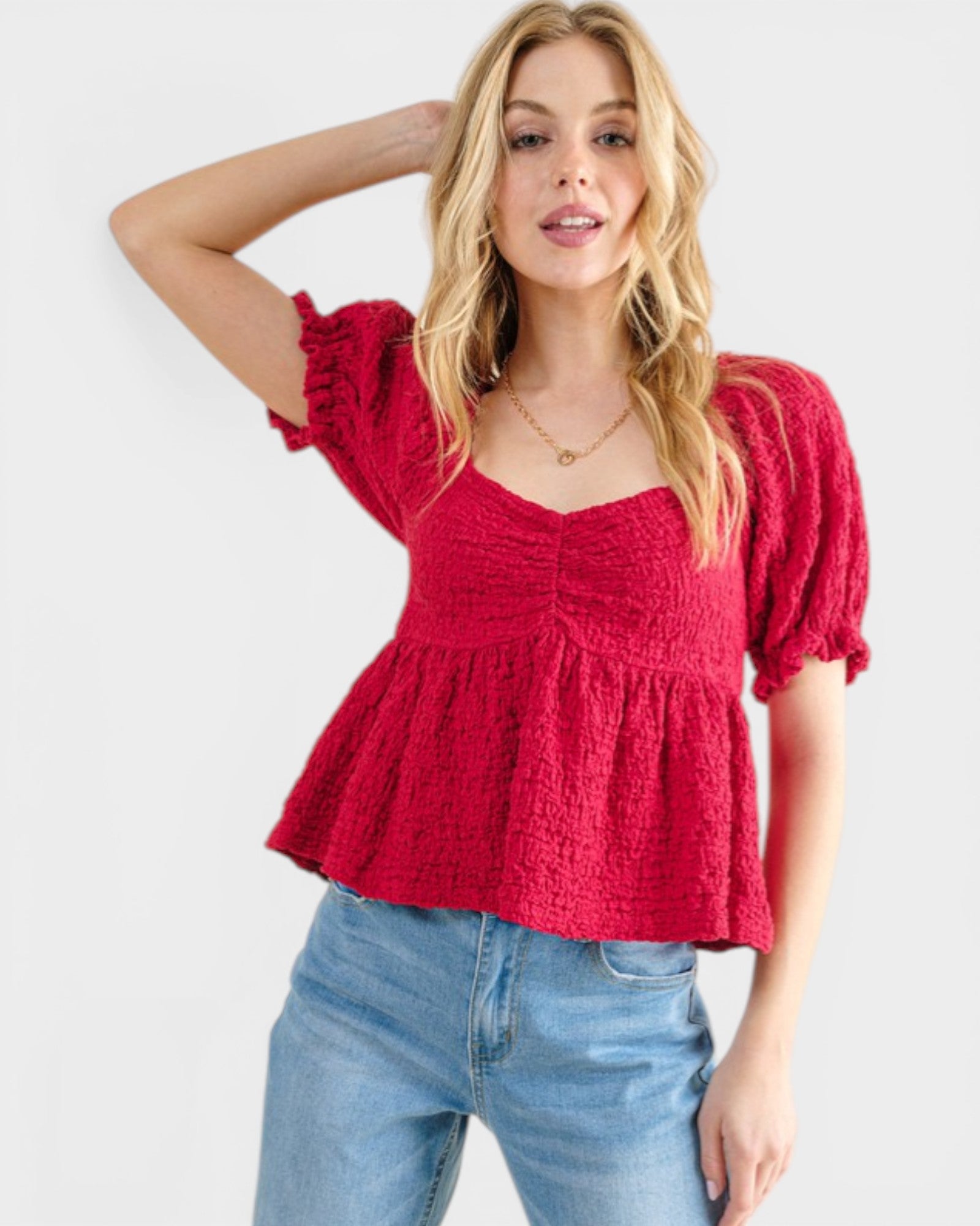 Woman wearing a red textured top and blue jeans on a white background