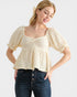 Woman wearing a beige textured blouse and blue jeans on a white background