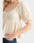 Woman wearing a light beige lace top with short sleeves on a white background