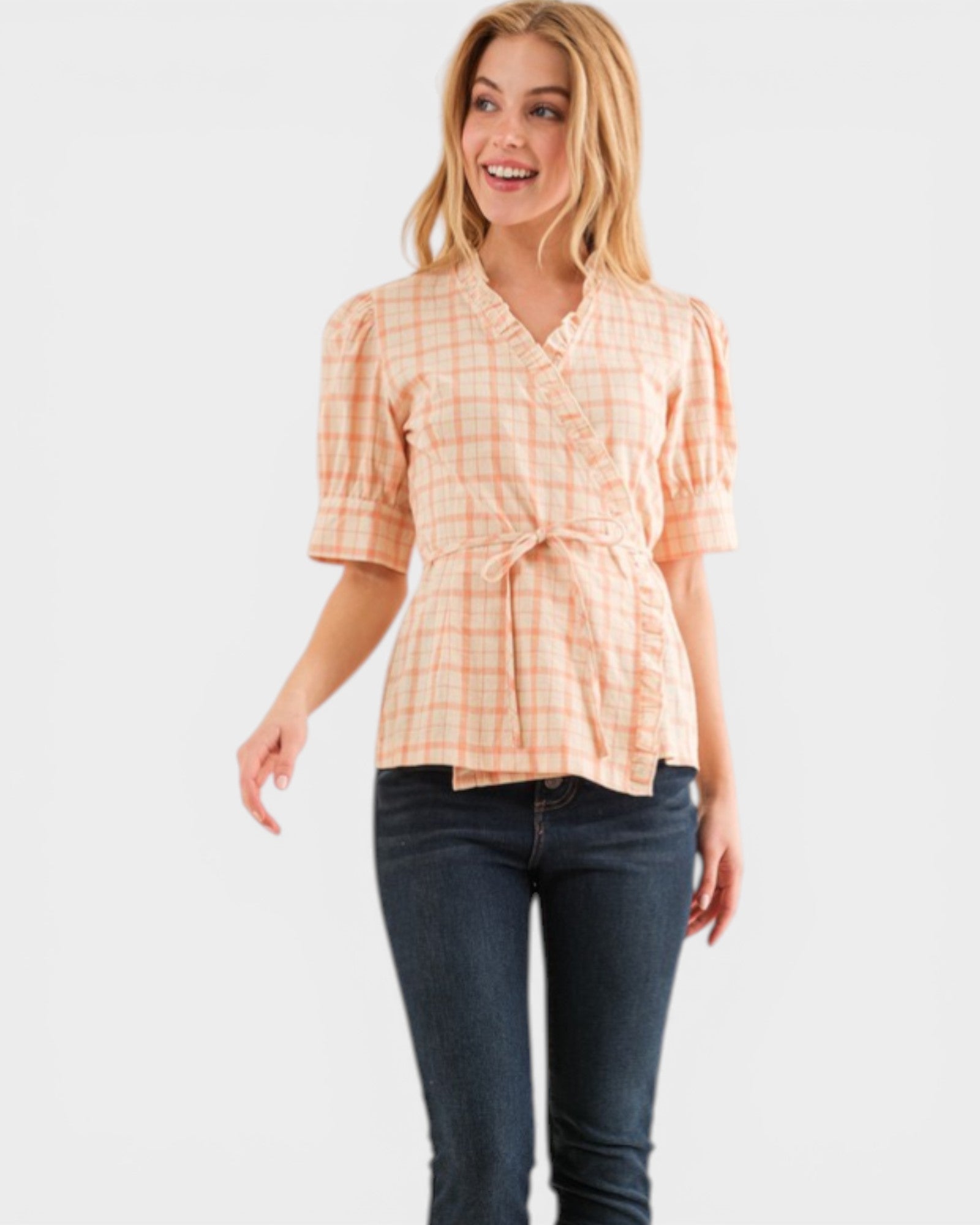Woman wearing a peach checkered blouse and blue jeans on a white background