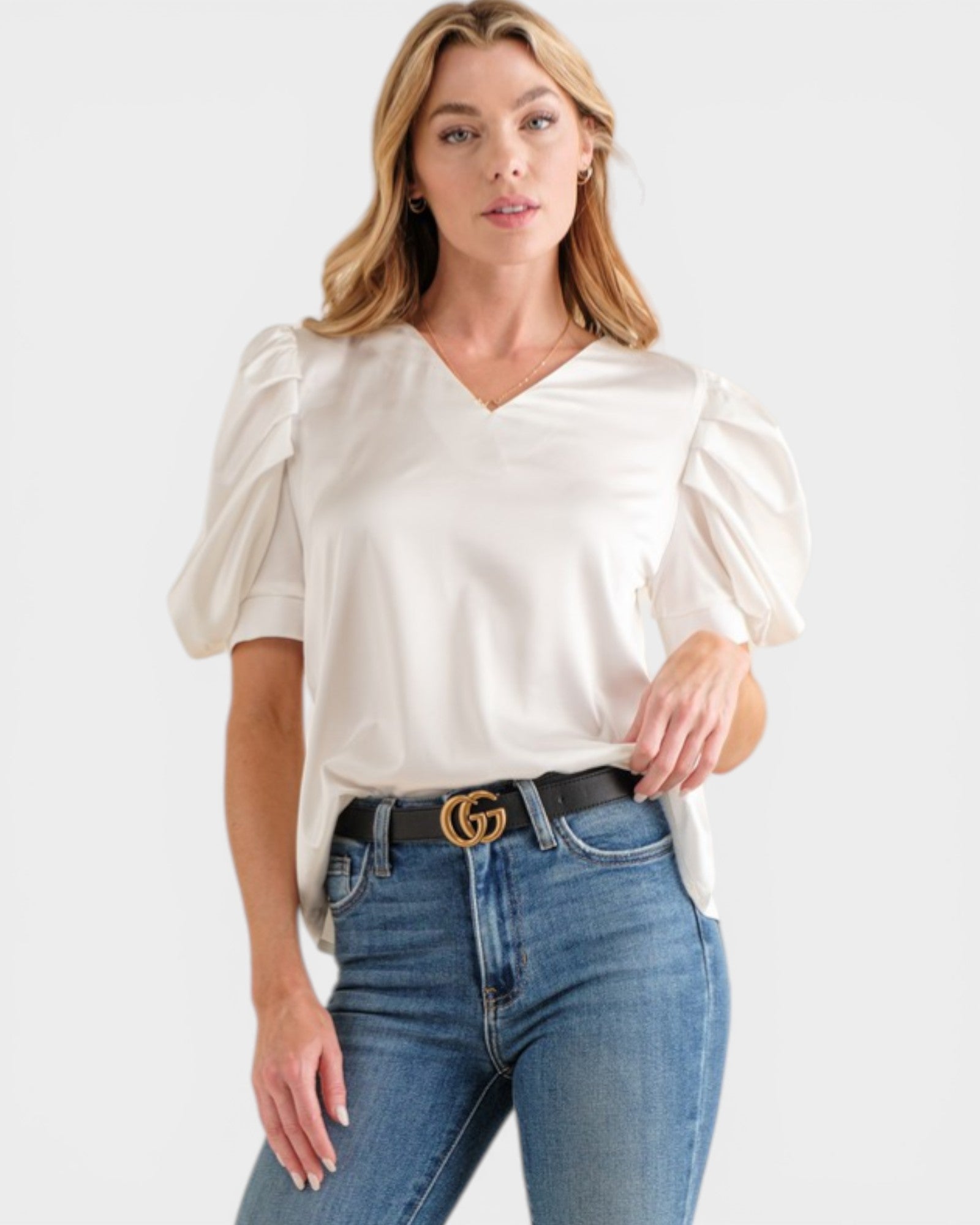 Woman wearing a white blouse with puff sleeves and blue jeans on a white background