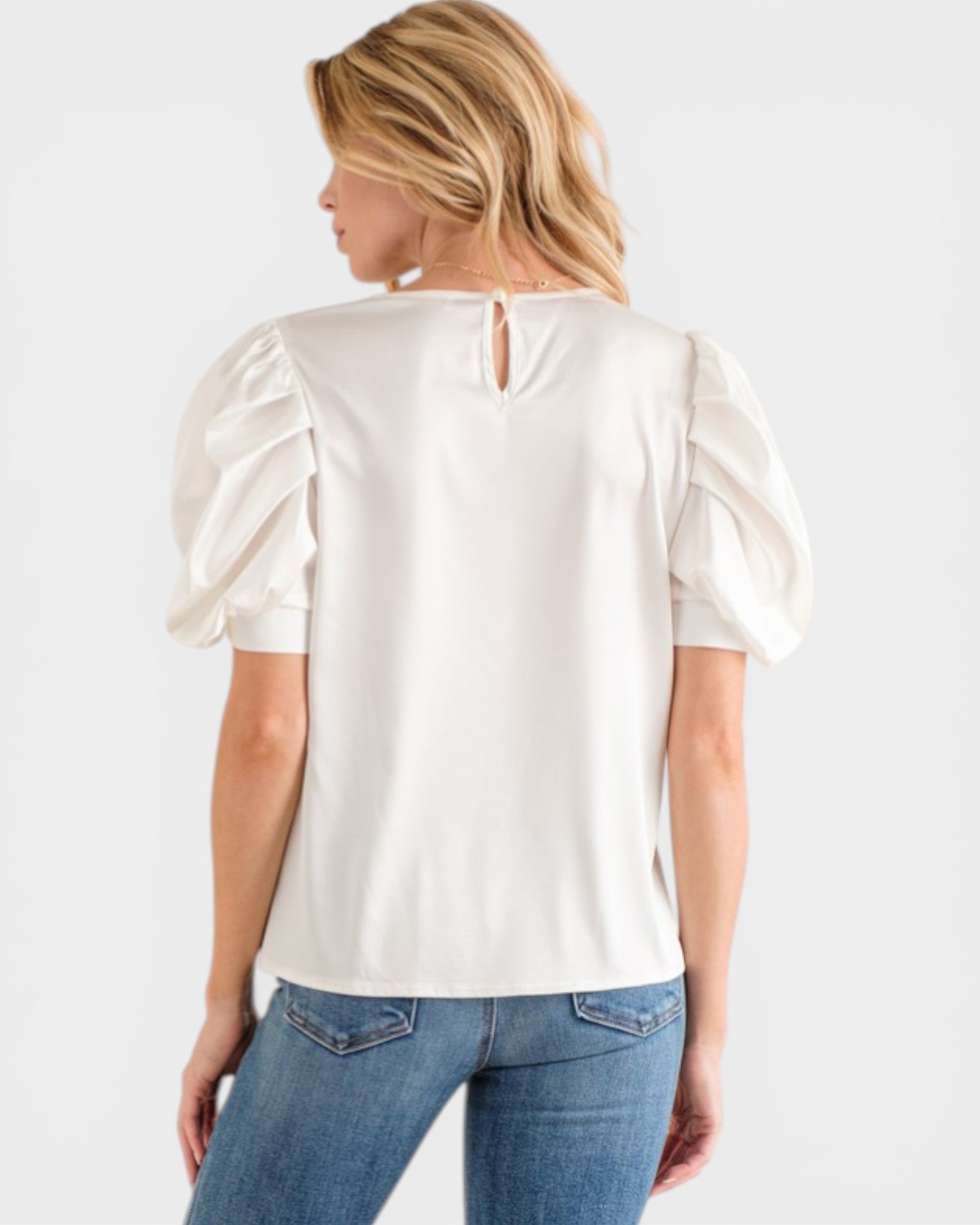 Woman wearing a white blouse with puff sleeves and blue jeans on a white background
