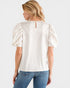 Woman wearing a white blouse with puff sleeves and blue jeans on a white background