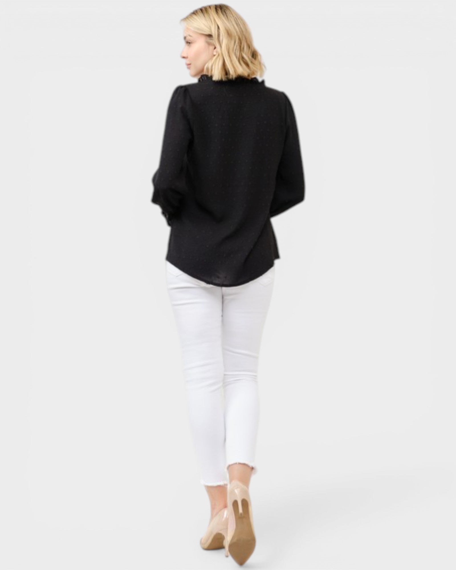 Woman wearing a black blazer and white pants on a plain background