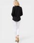 Woman wearing a black blazer and white pants on a plain background