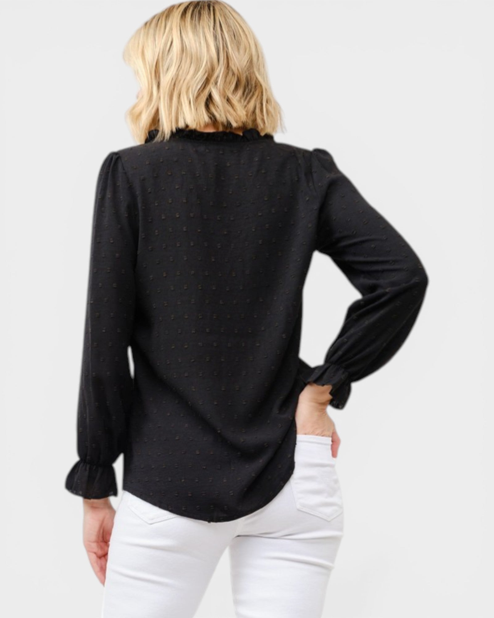 Person wearing a black long-sleeve top with white pants on a light gray background