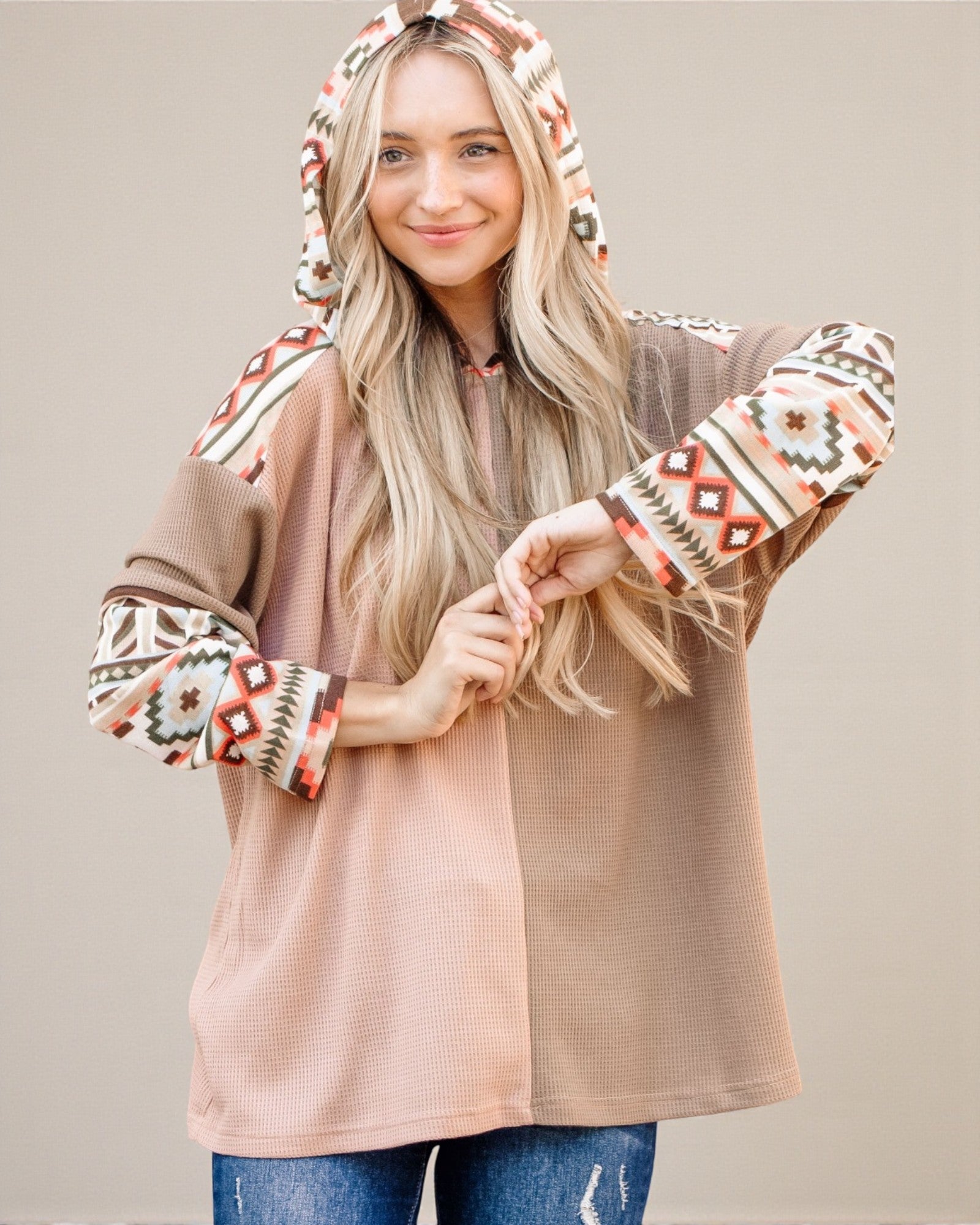 Woman wearing a beige cardigan with patterned sleeves and hood on a plain background