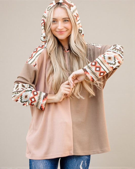 Woman wearing a beige cardigan with patterned sleeves and hood on a plain background
