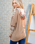 Woman wearing a beige sweater with patterned sleeves against a tiled wall.
