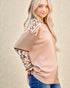 Woman wearing a beige sweater with patterned sleeves against a beige background