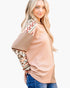 A woman wearing a peach-colored waffle-knit top with patterned raglan sleeves, paired with blue jeans, photographed against a plain white background.