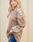 Woman wearing a brown and patterned long-sleeve top against a beige wall.