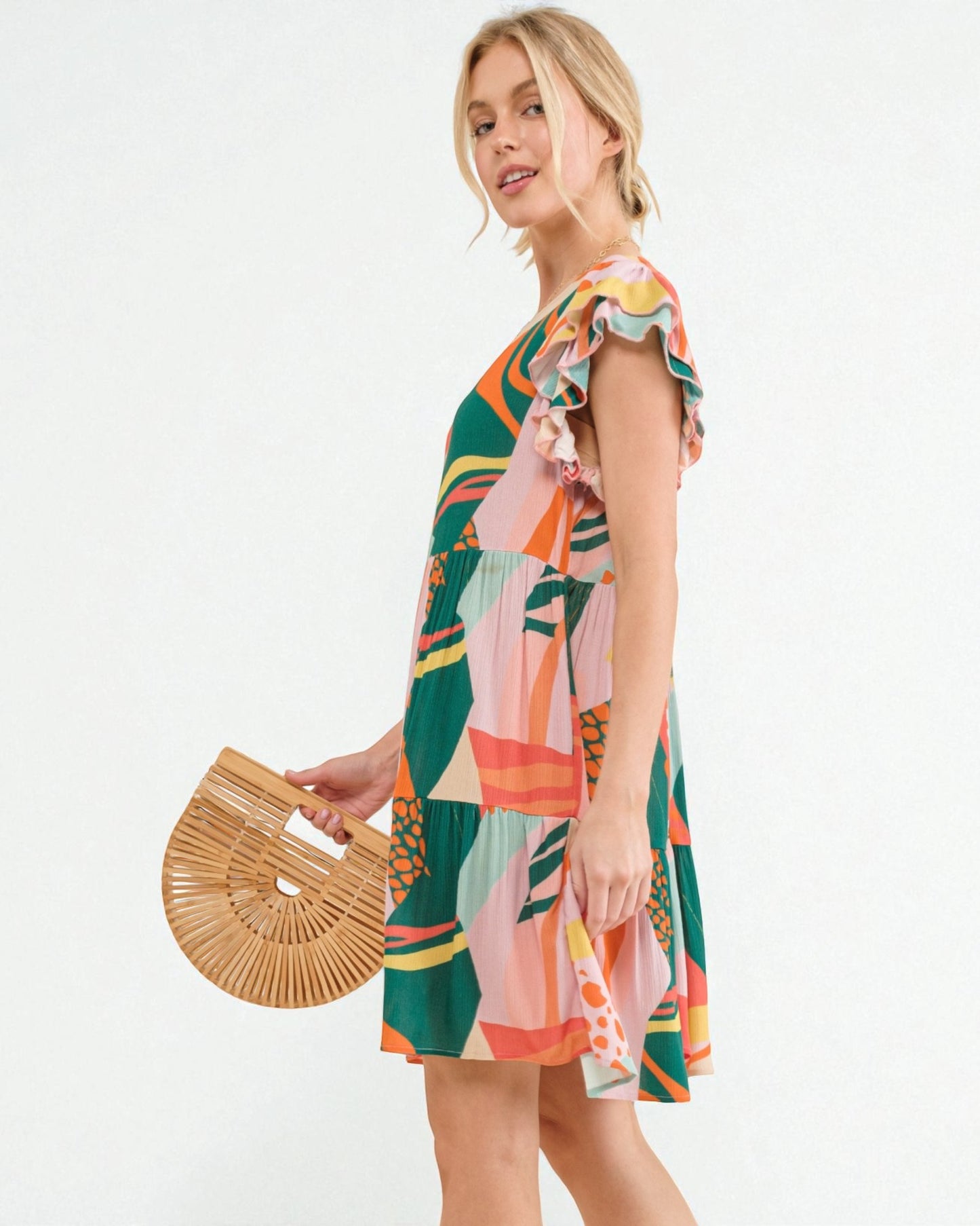 Woman wearing a colorful patterned dress holding a woven bag on a white background
