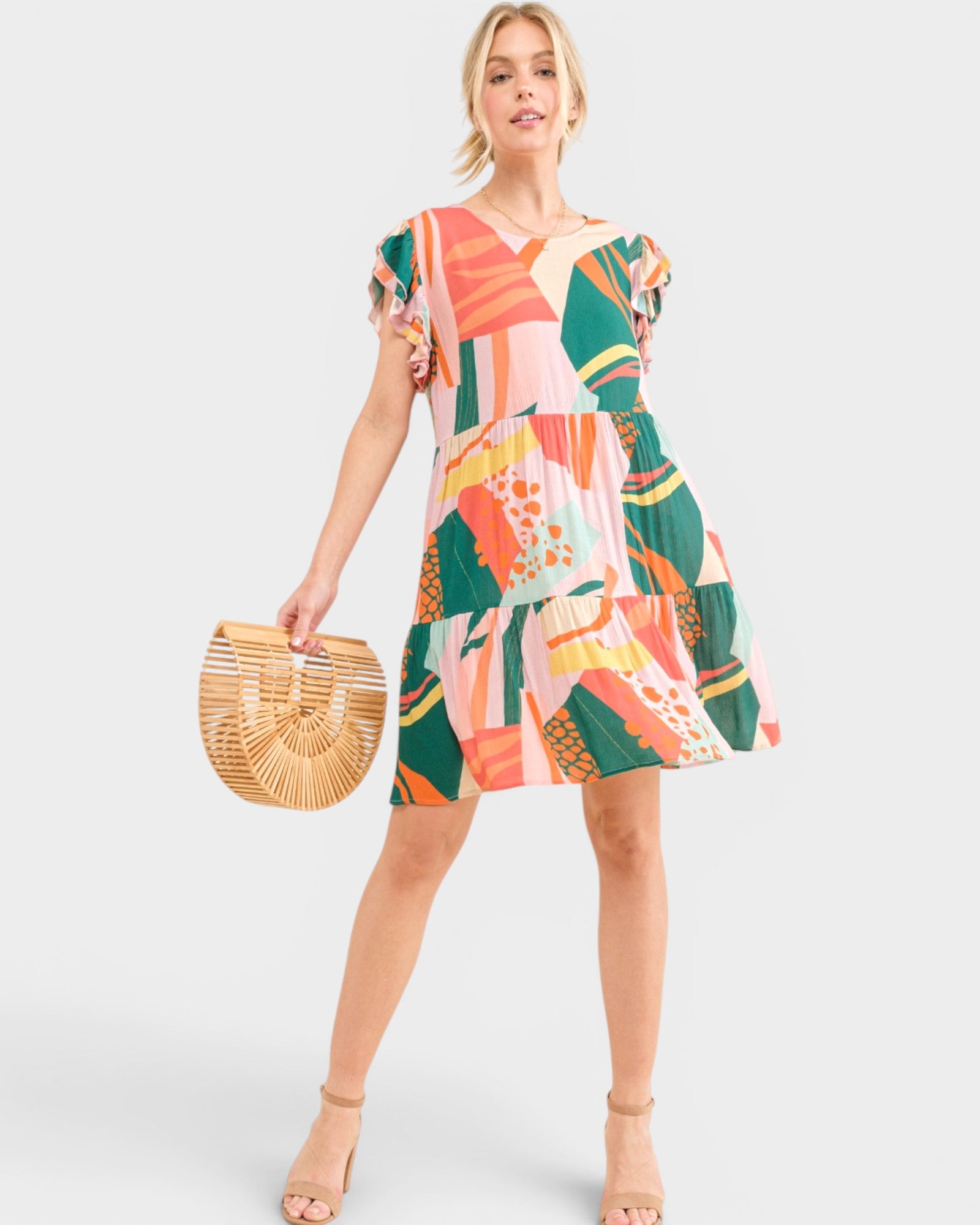Woman wearing a colorful patterned dress holding a woven bag on a white background