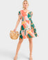 Woman wearing a colorful patterned dress holding a woven bag on a white background