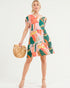 Woman wearing a colorful patterned dress holding a woven handbag on a white background