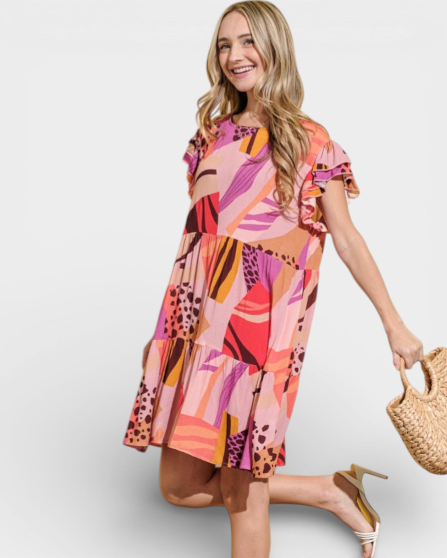 Woman wearing a colorful patterned dress holding a straw bag on a plain background