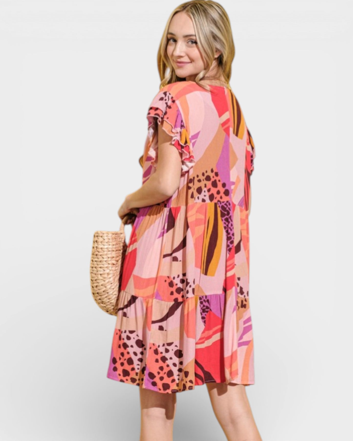 Woman wearing a colorful patterned dress holding a straw bag on a white background