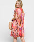 Woman wearing a colorful patterned dress holding a straw bag on a white background