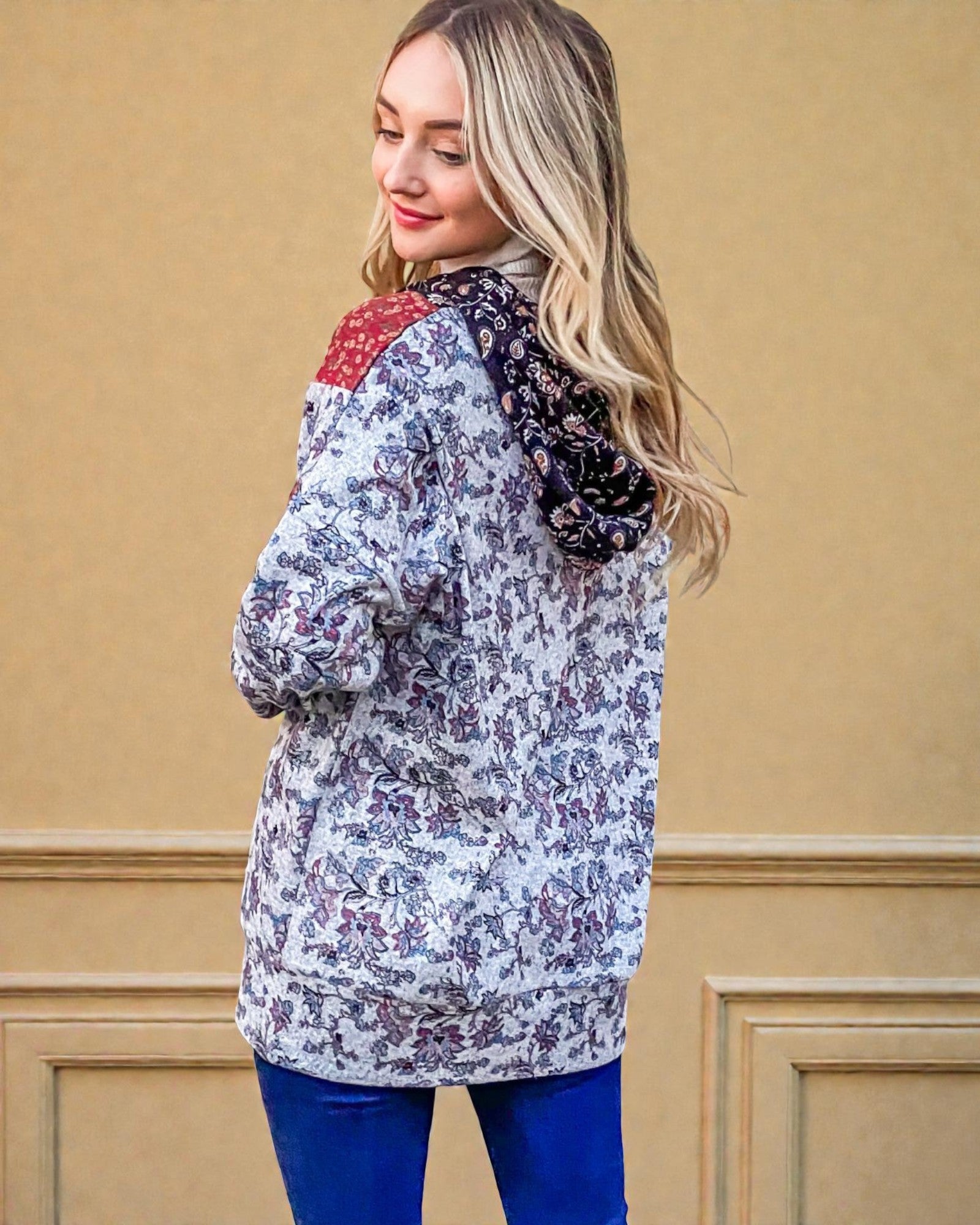 Woman wearing a floral jacket with a red patch on a beige wall background