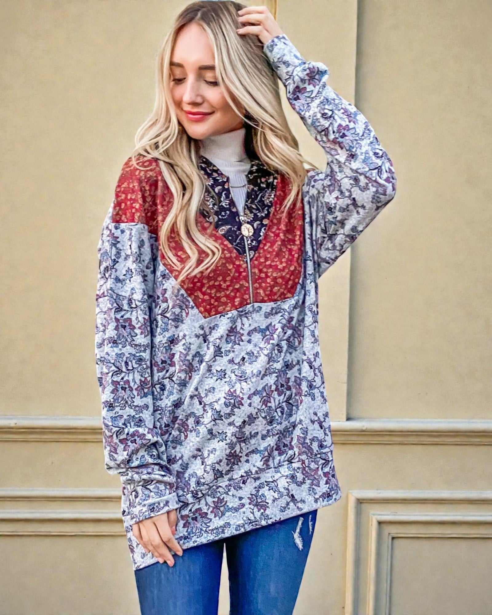 Woman wearing a colorful floral and patchwork jacket against a beige wall.