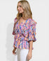 Woman wearing a colorful patterned blouse against a white background