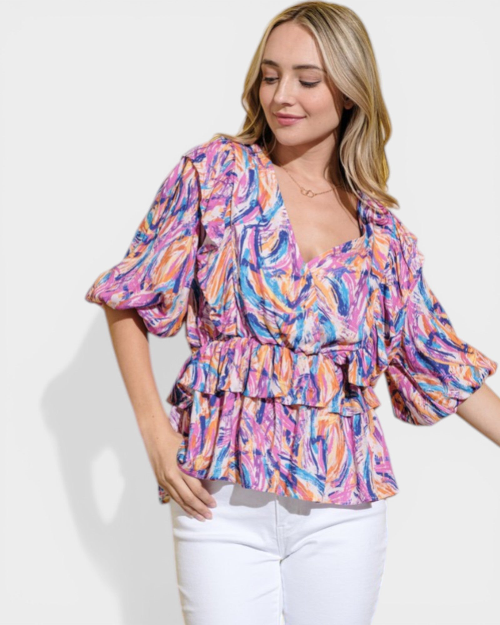 Woman wearing a colorful patterned top with white pants on a light background