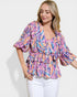 Woman wearing a colorful patterned top with white pants on a light background