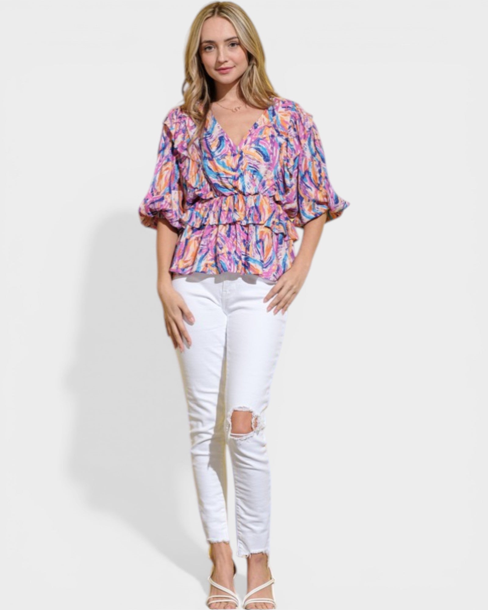 Woman wearing a colorful blouse and white pants on a plain background
