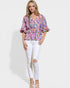 Woman wearing a colorful blouse and white pants on a plain background