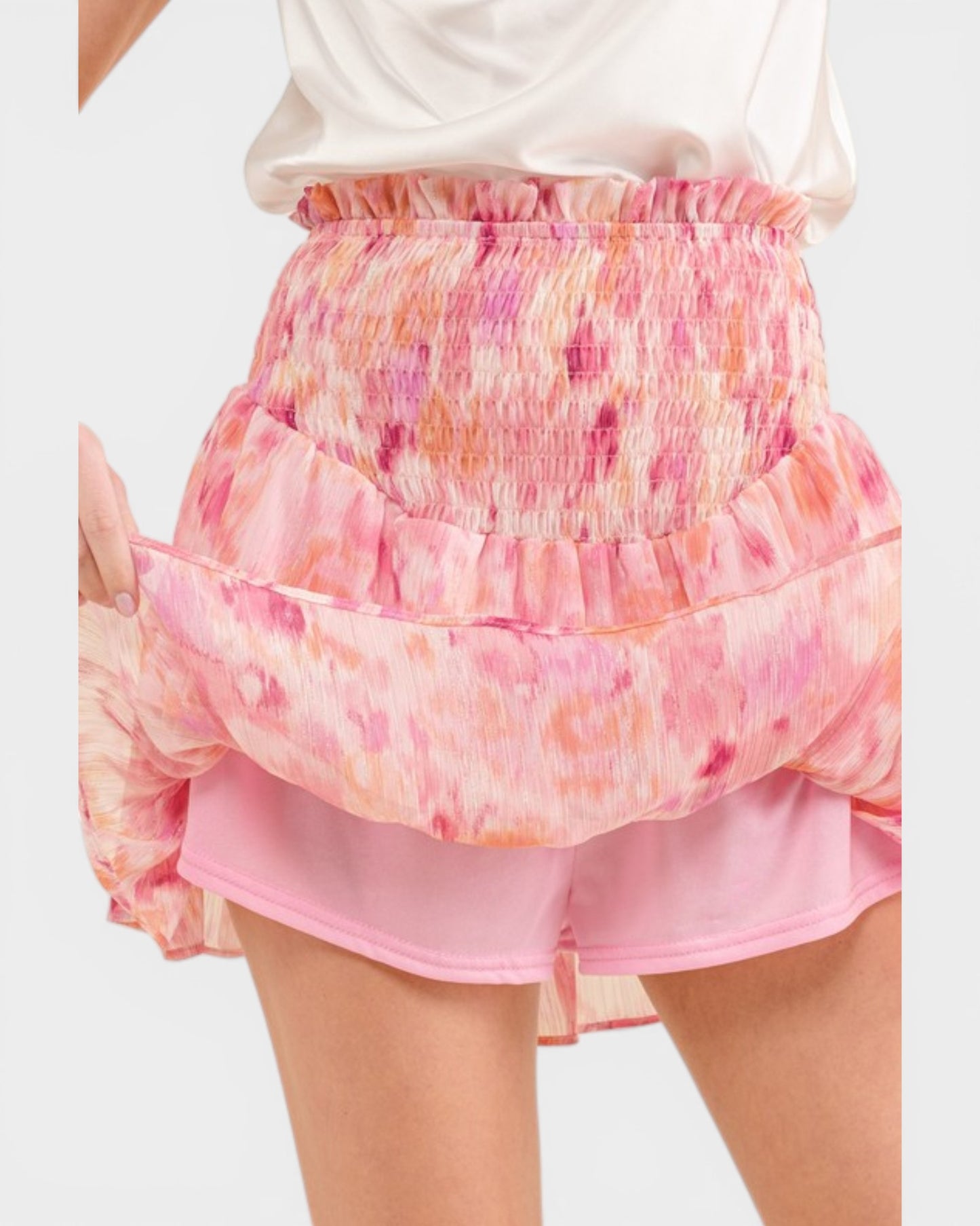 Pink tiered skirt with floral pattern worn over a white top on a plain background