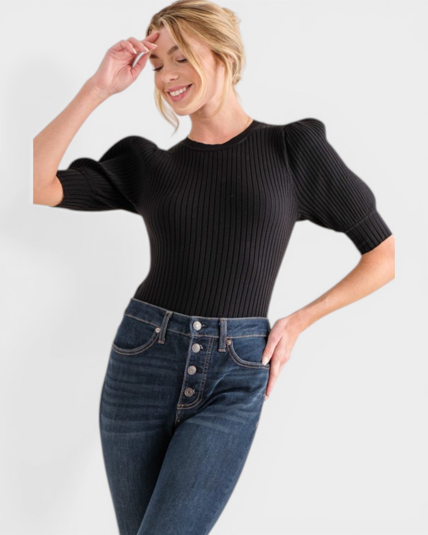 Woman wearing a black ribbed sweater and blue jeans on a white background