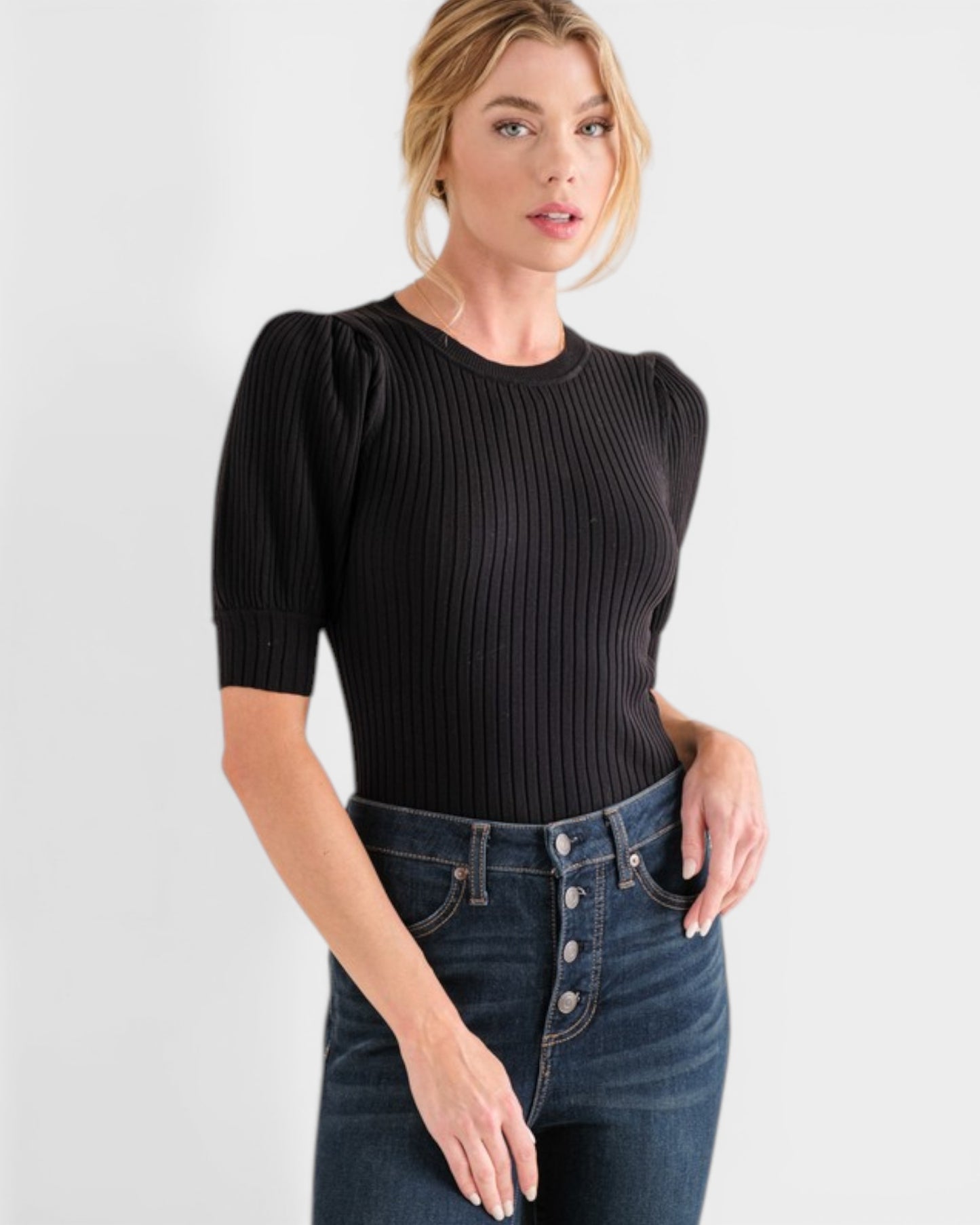 Woman wearing a black ribbed top and blue jeans on a light gray background
