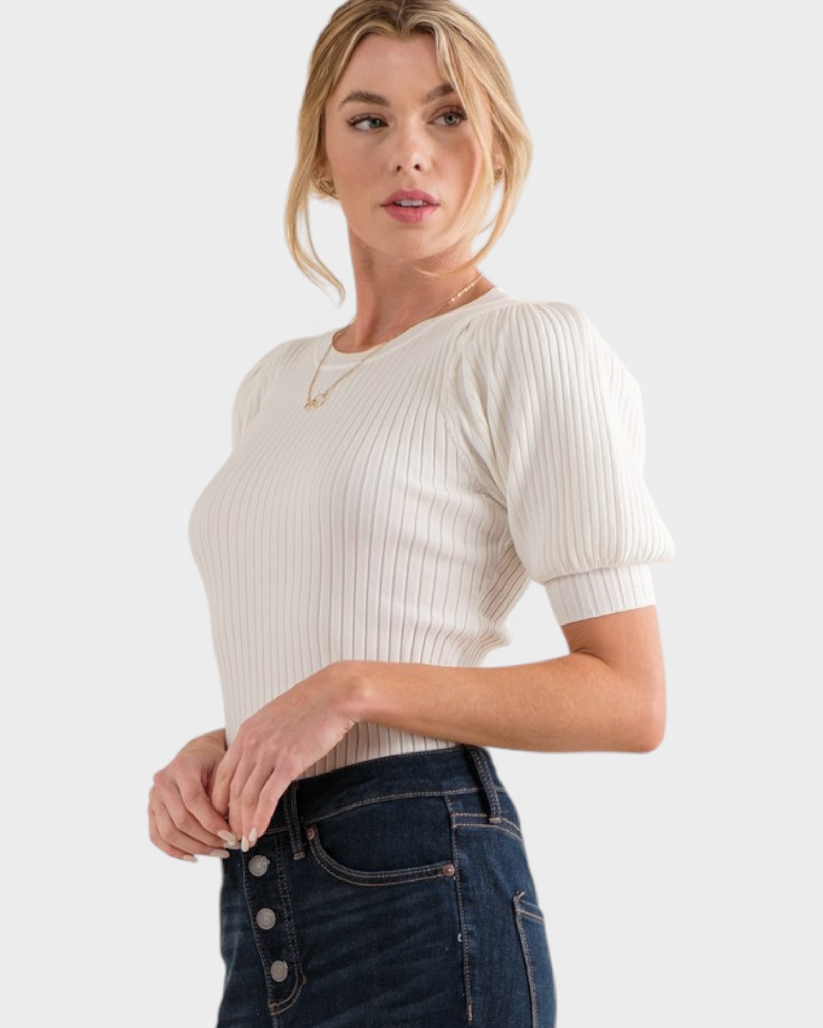 Woman wearing a white ribbed sweater and blue jeans on a white background
