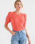 Woman wearing a coral ribbed top and blue jeans on a white background