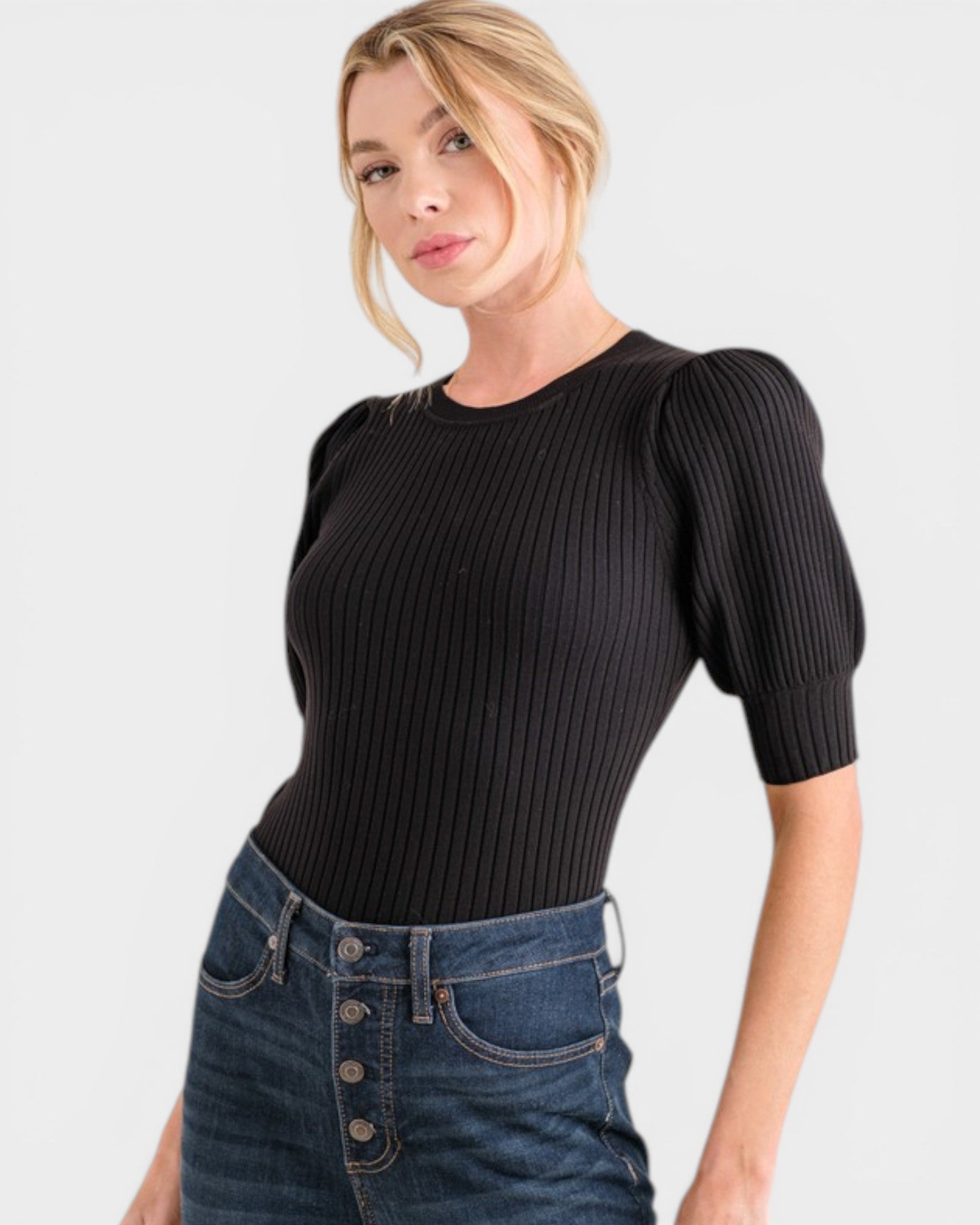 Woman wearing a black ribbed top with puff sleeves and blue jeans on a white background