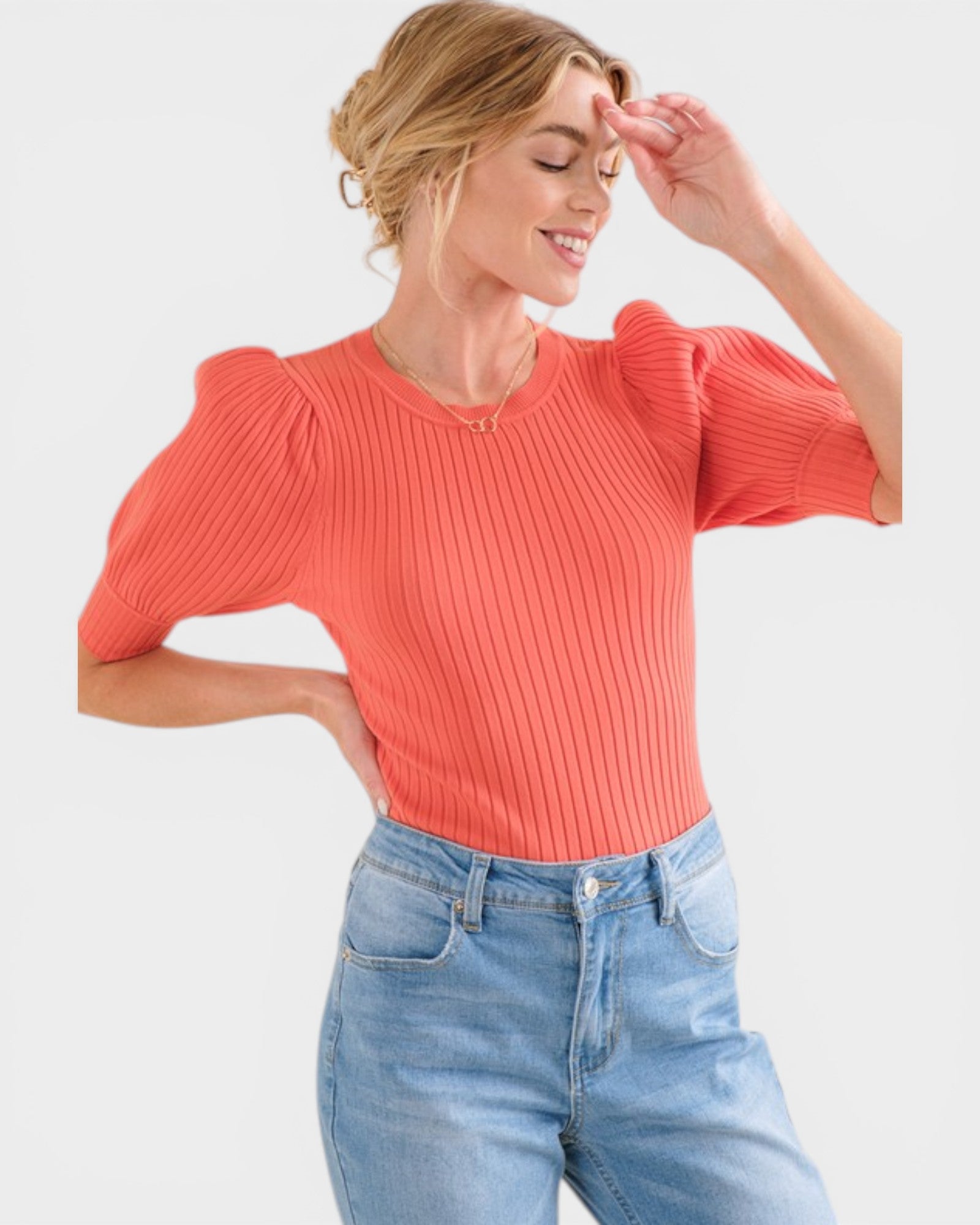 Woman wearing a coral ribbed top and blue jeans on a light gray background