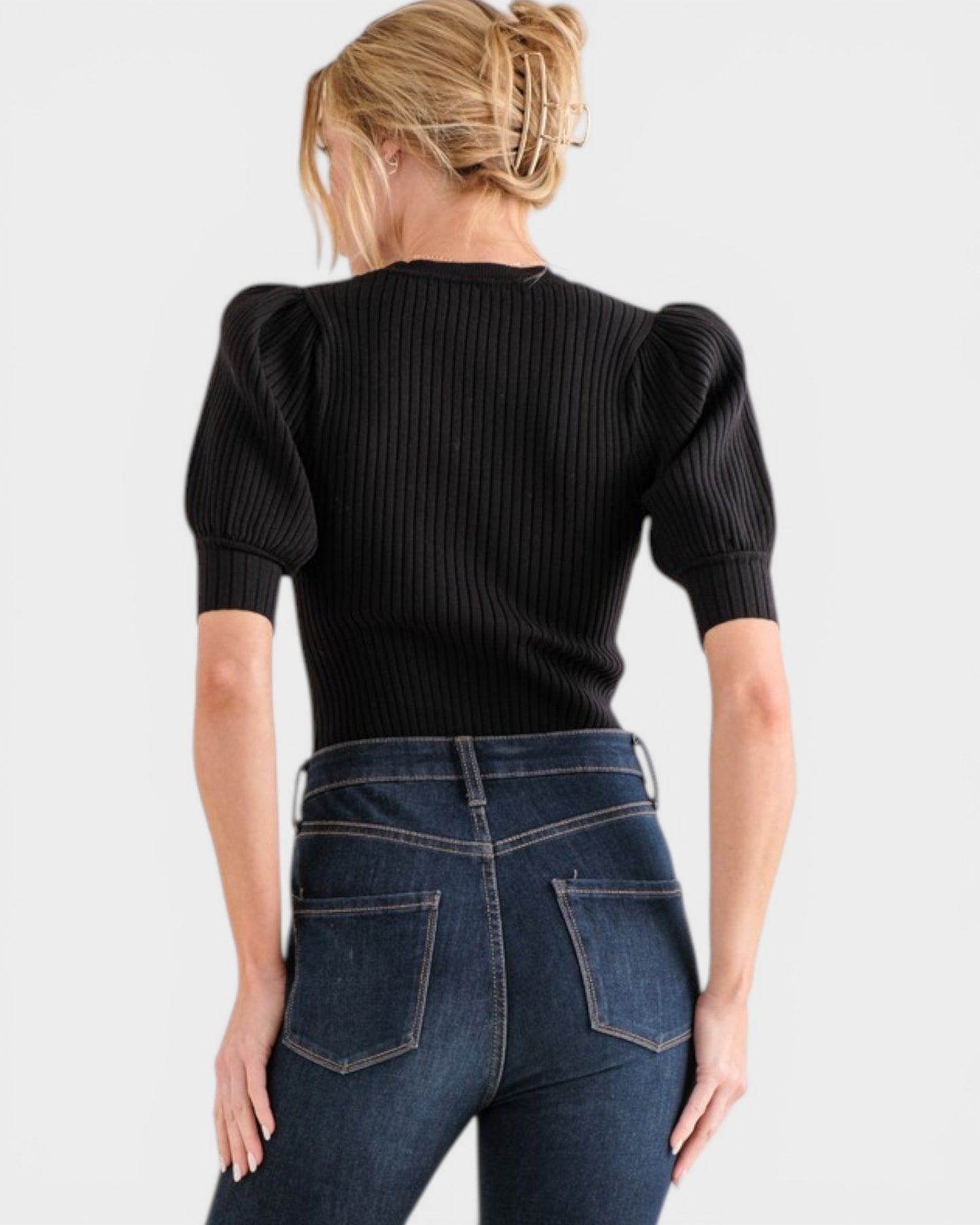Person wearing a black ribbed sweater and blue jeans on a white background