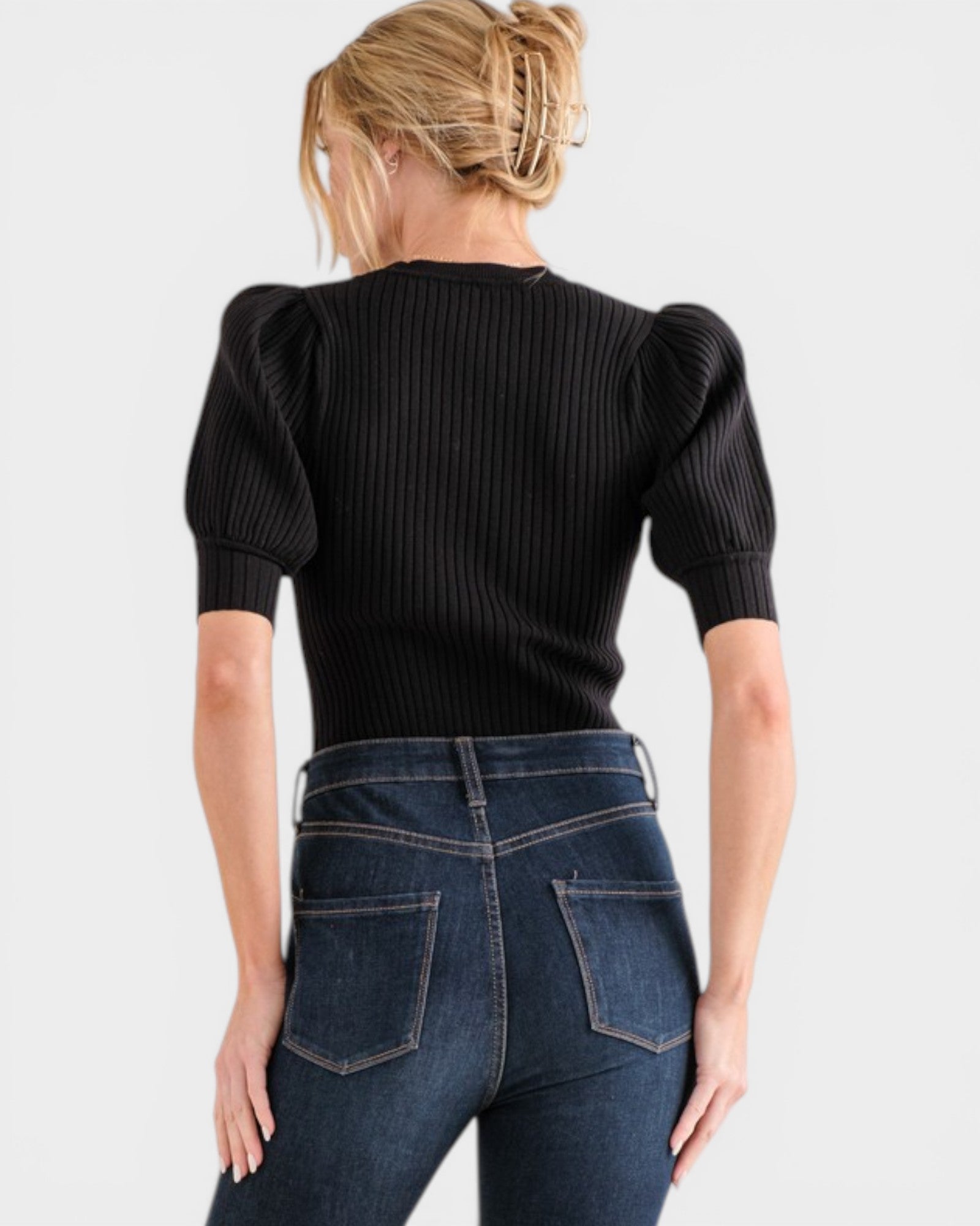 Person wearing a black ribbed sweater and blue jeans on a white background