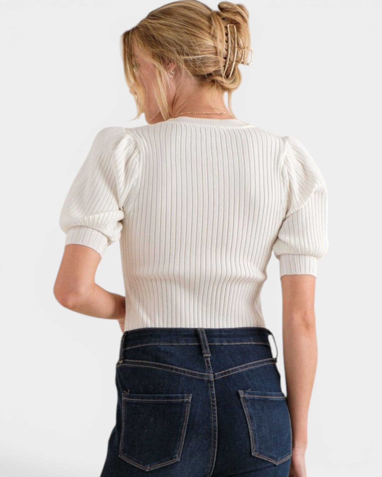 Person wearing a white ribbed sweater and blue jeans on a plain background