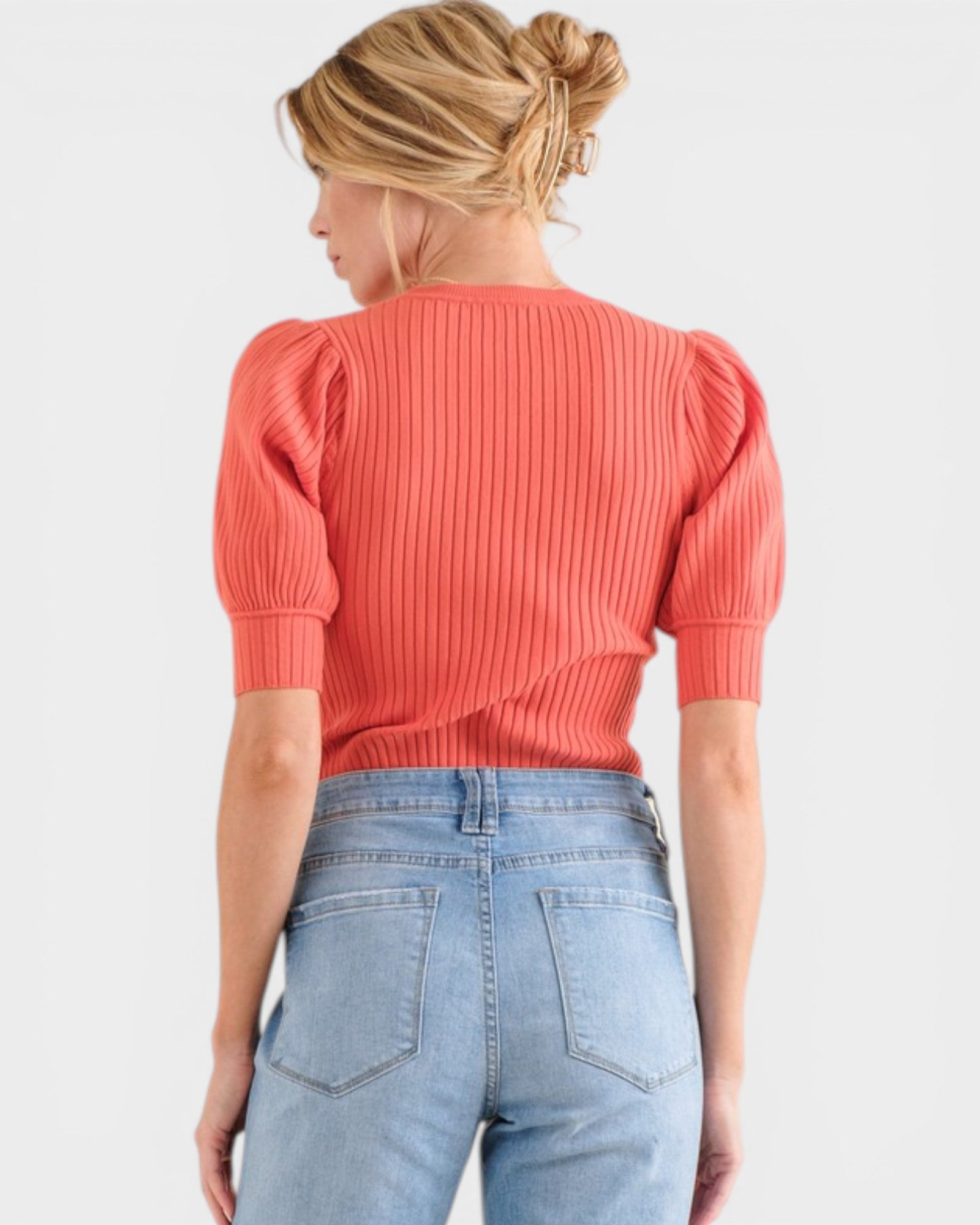 Woman wearing a coral ribbed top with puff sleeves and light blue jeans on a white background