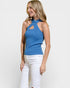 Woman wearing a blue sleeveless top with cut-out design and white pants on a plain background