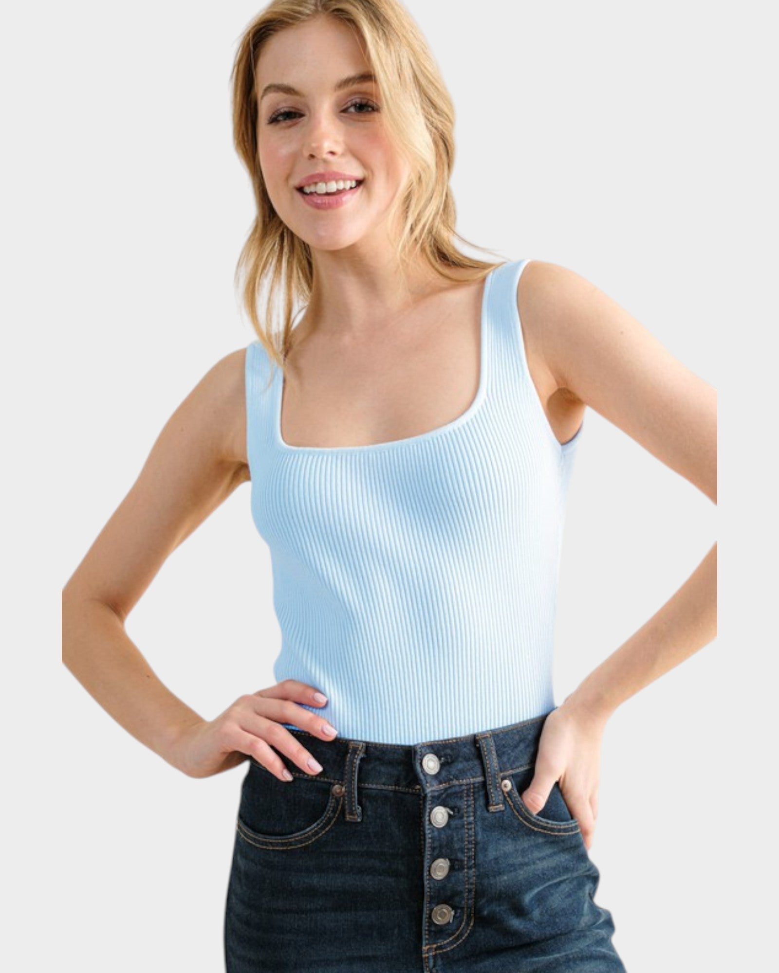 Woman wearing a light blue tank top and dark blue jeans on a white background