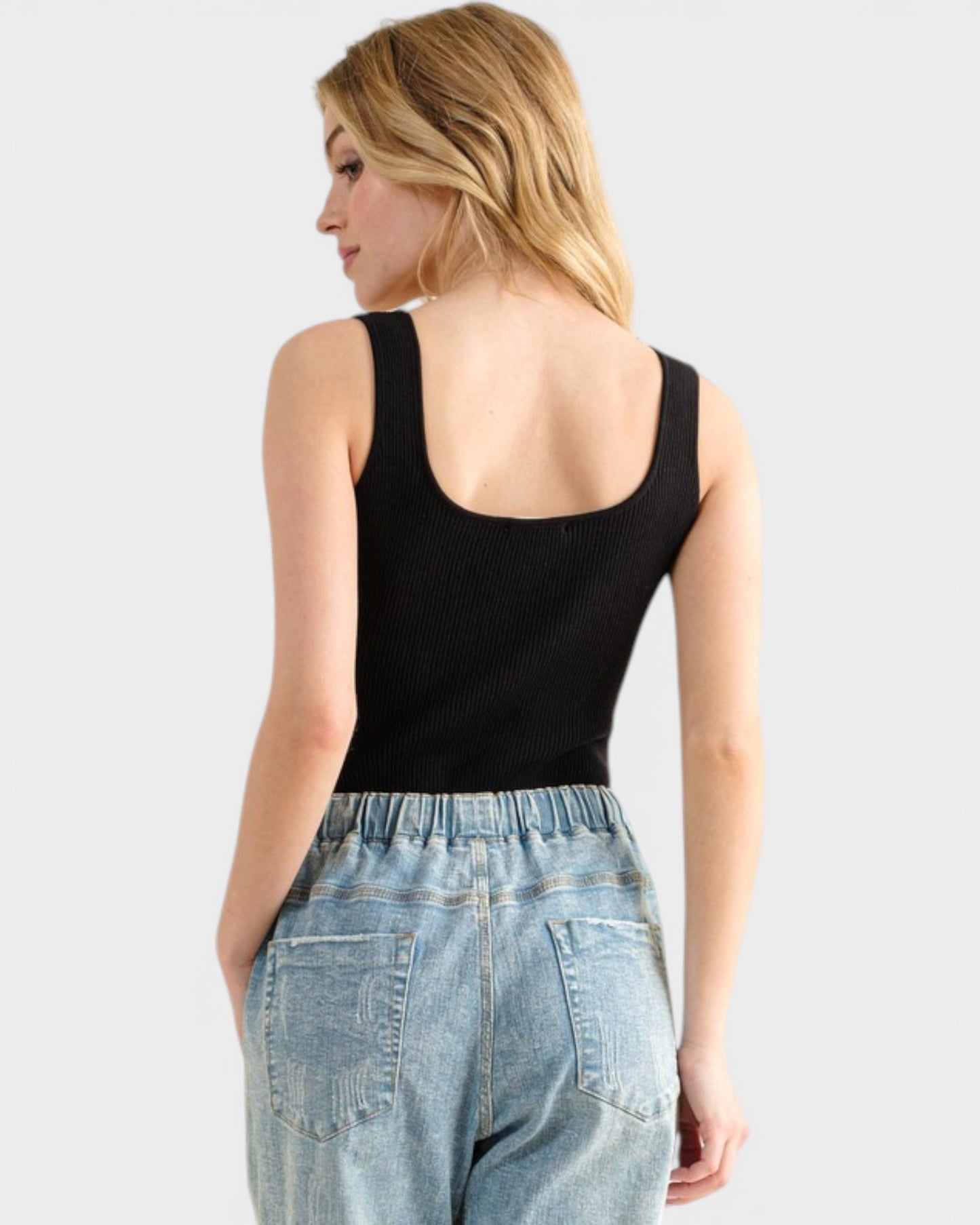 Woman wearing a black tank top and light blue jeans on a plain background